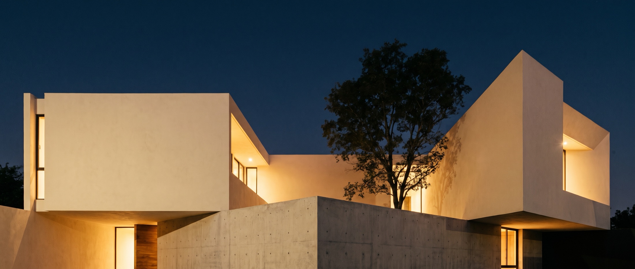 Volúmenes de arquitectura contemporánea en crema y concreto bajo un cielo azul profundo al caer la tarde
